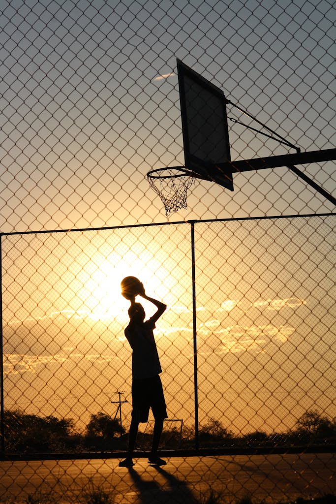 Silhouetted athlete playing basketball on an outdoor court with a vibrant sunset backdrop.